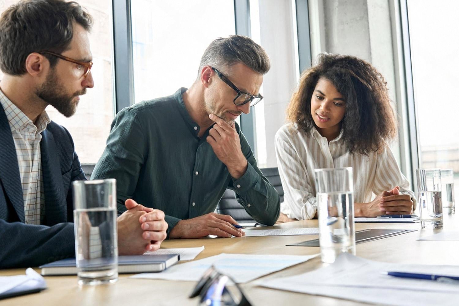 Three business professionals reviewing partnership contract documents around a boardroom table in a UAE office